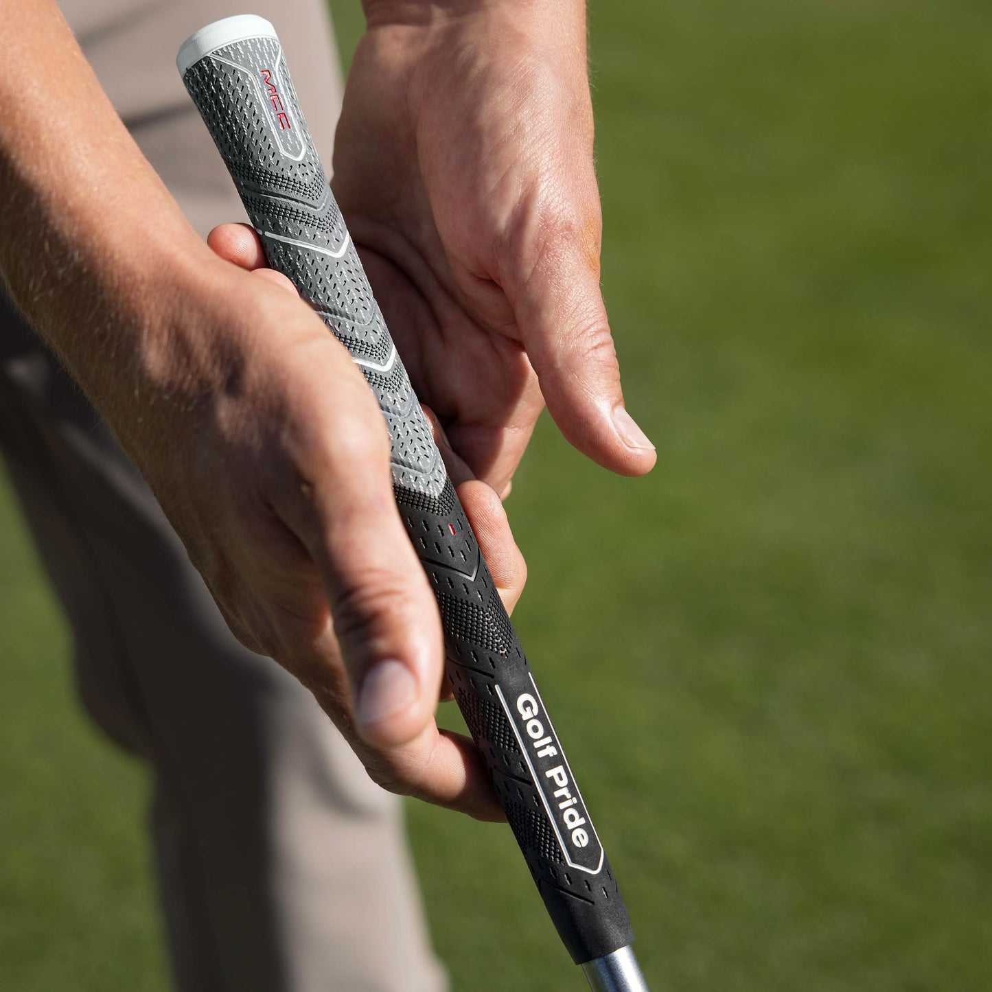 Close-up of a hand holding a golf club with a Golf Pride grip on a blurred green background