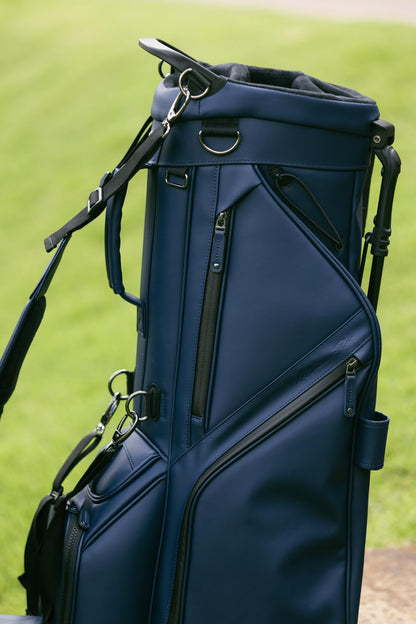 Navy blue golf bag with black straps on a grassy background
