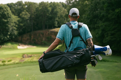 Man carrying a golf bag on a golf course with trees in the background