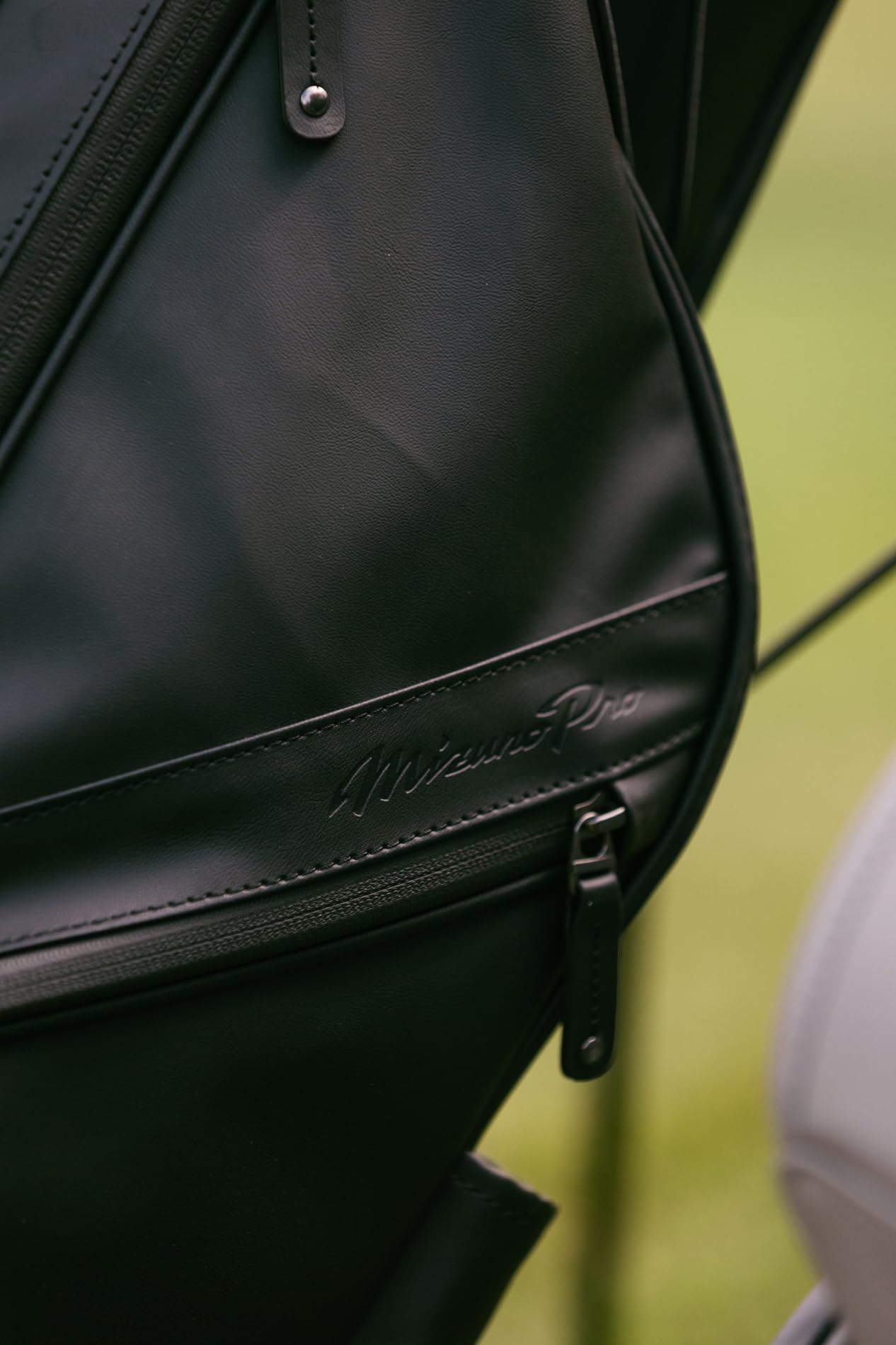 Close-up of a black leather bag with a brand logo on a blurred green background