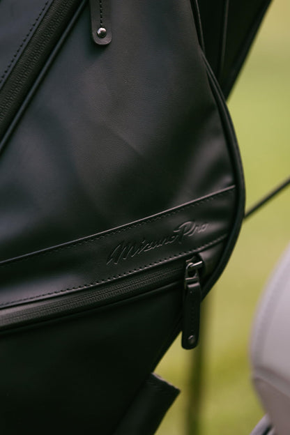 Close-up of a black leather bag with a brand logo on a blurred green background