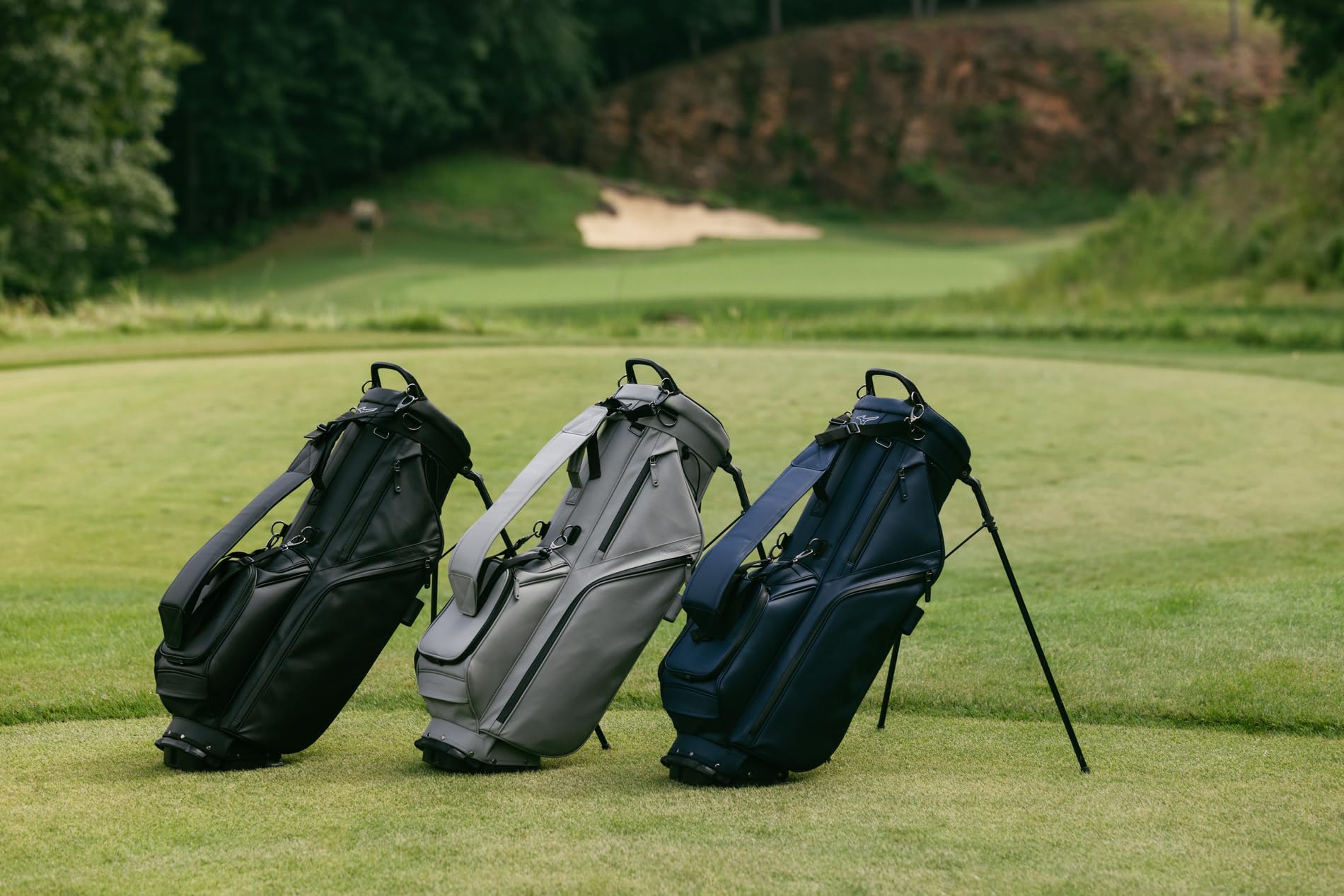 Three golf bags on a grassy area with a golf course background