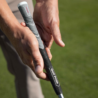 Close-up of a hand holding a golf club with a Golf Pride grip on a blurred green background