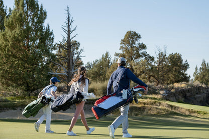Three people walking on a golf course carrying golf bags.