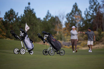 Two golf carts with bags on a golf course with two people interacting.
