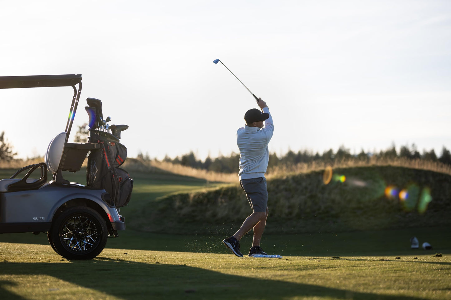 Golfer swinging a club on a golf course with a cart in the background