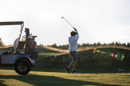 Golfer swinging a club on a golf course with a cart in the background