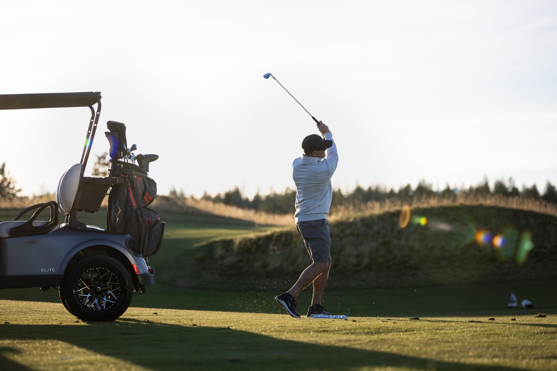 Golfer swinging a club on a golf course with a cart in the background