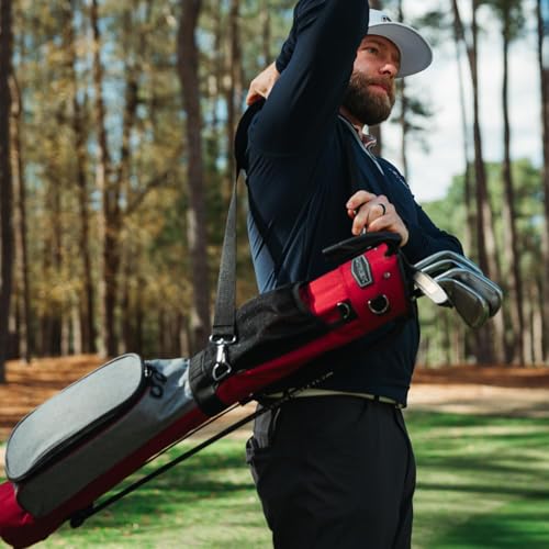 Man holding a red golf bag on a golf course with trees in the background