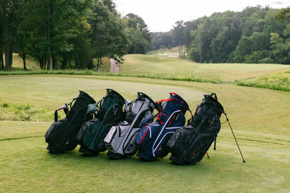 Five golf bags on a grassy area with trees in the background