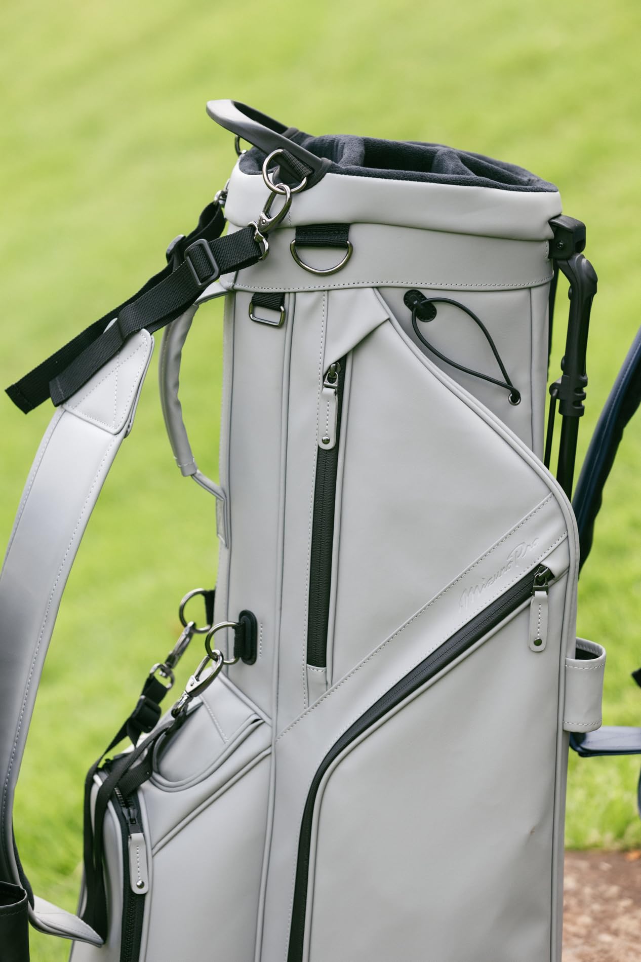 Close-up of a gray golf bag with black zippers on a grassy background
