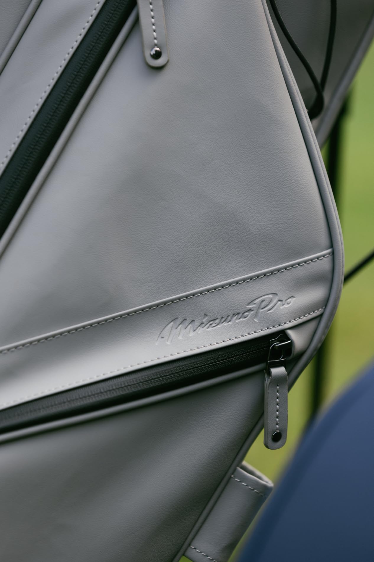 Close-up of a gray leather bag with a visible brand logo on a blurred green background